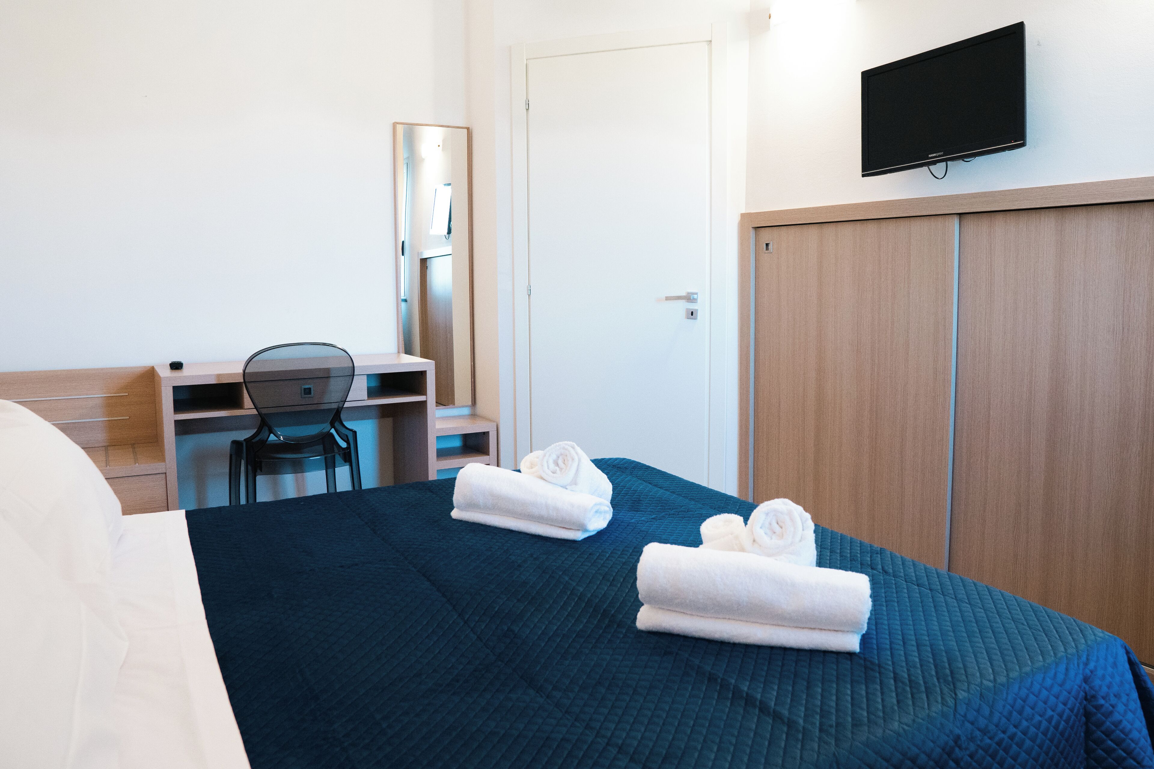 A hotel room with a bed, a desk, a chair, a television, and a wardrobe.