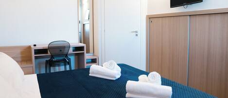 A hotel room with a bed, a desk, a chair, a television, and a wardrobe.