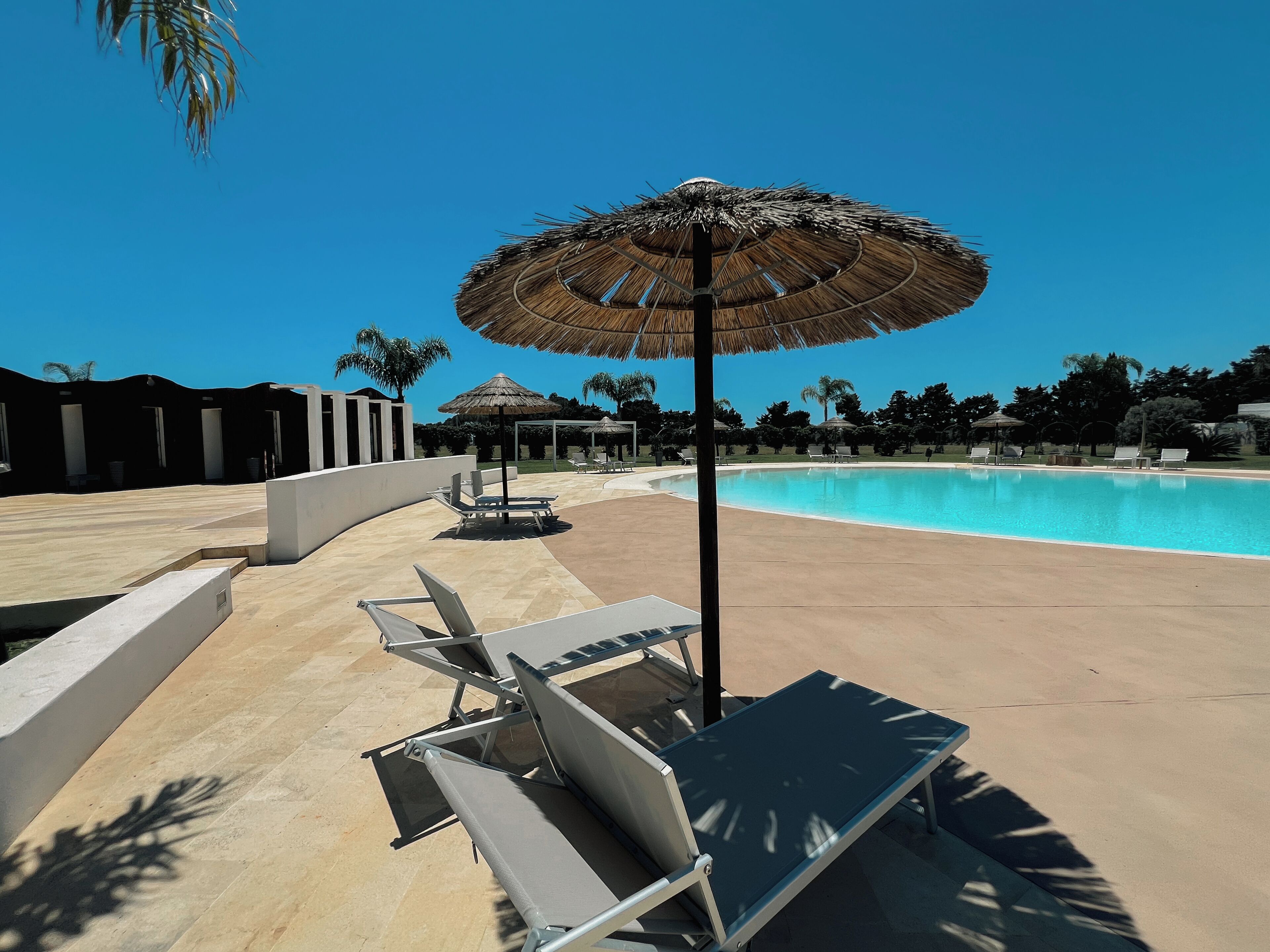 A poolside area with lounge chairs and a thatched umbrella.