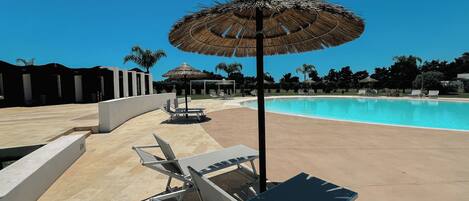 A poolside area with lounge chairs and a thatched umbrella.