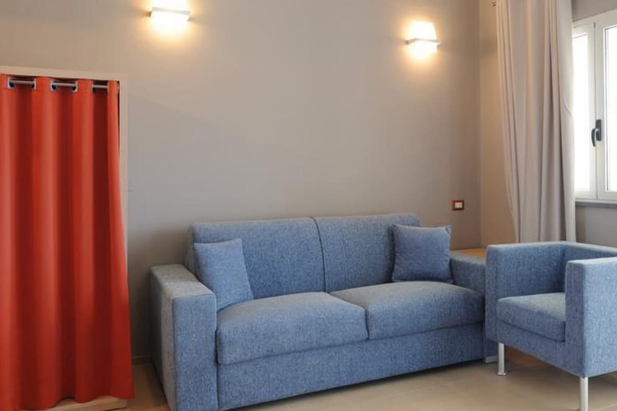 A room with a light blue sofa, a matching armchair, a red curtain, and a window with curtains.