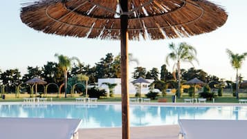 A poolside area with two sun loungers, a table with a drink, and a thatched umbrella.