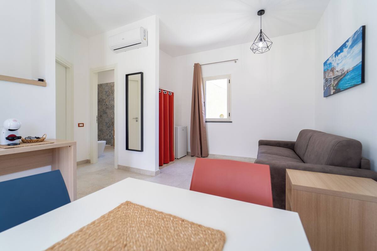 Um quarto moderno e bem iluminado, com sofá, mesa de jantar e cozinha.