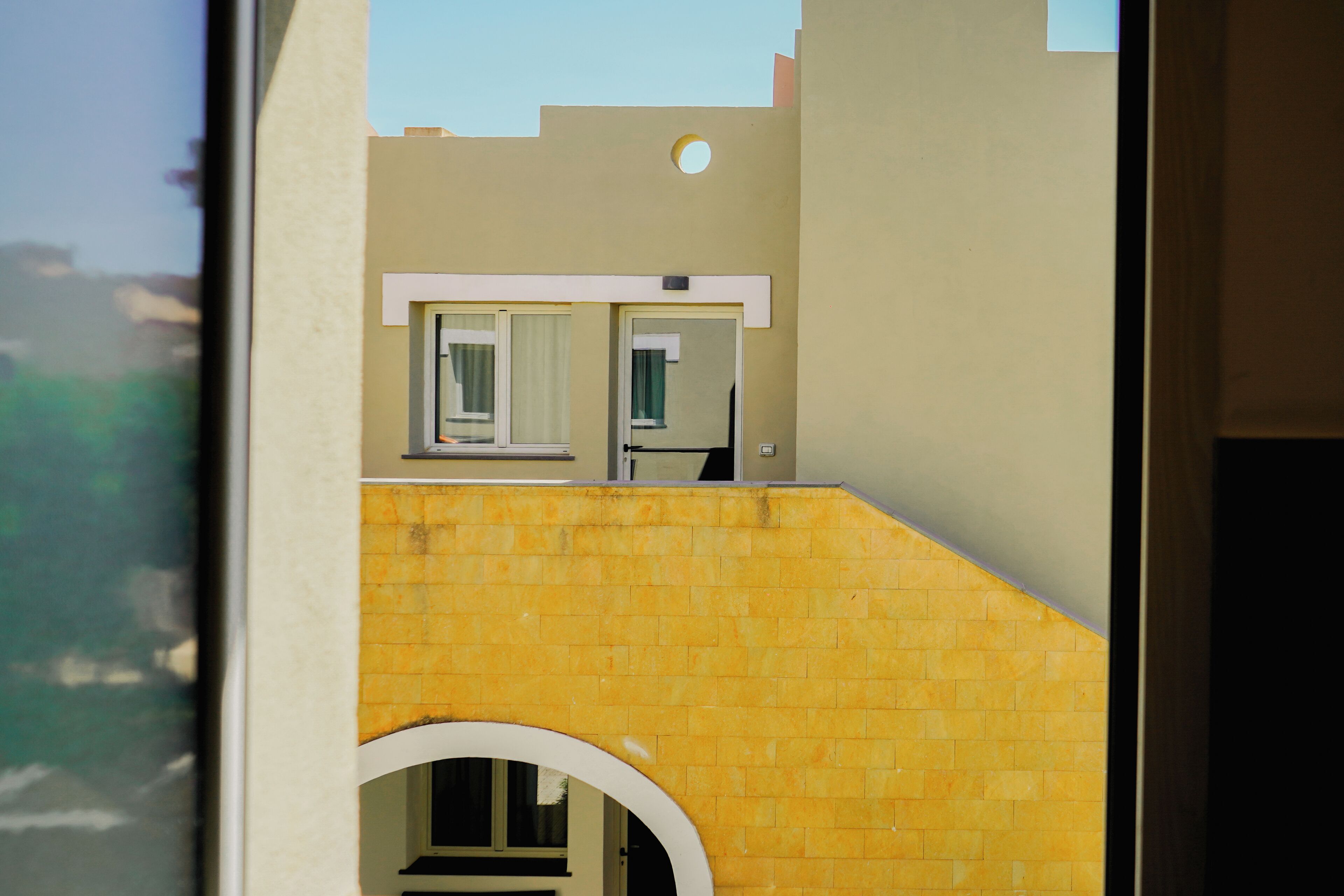 Une vue d’un bâtiment avec un mur en briques jaunes, une fenêtre circulaire blanche et une porte.
