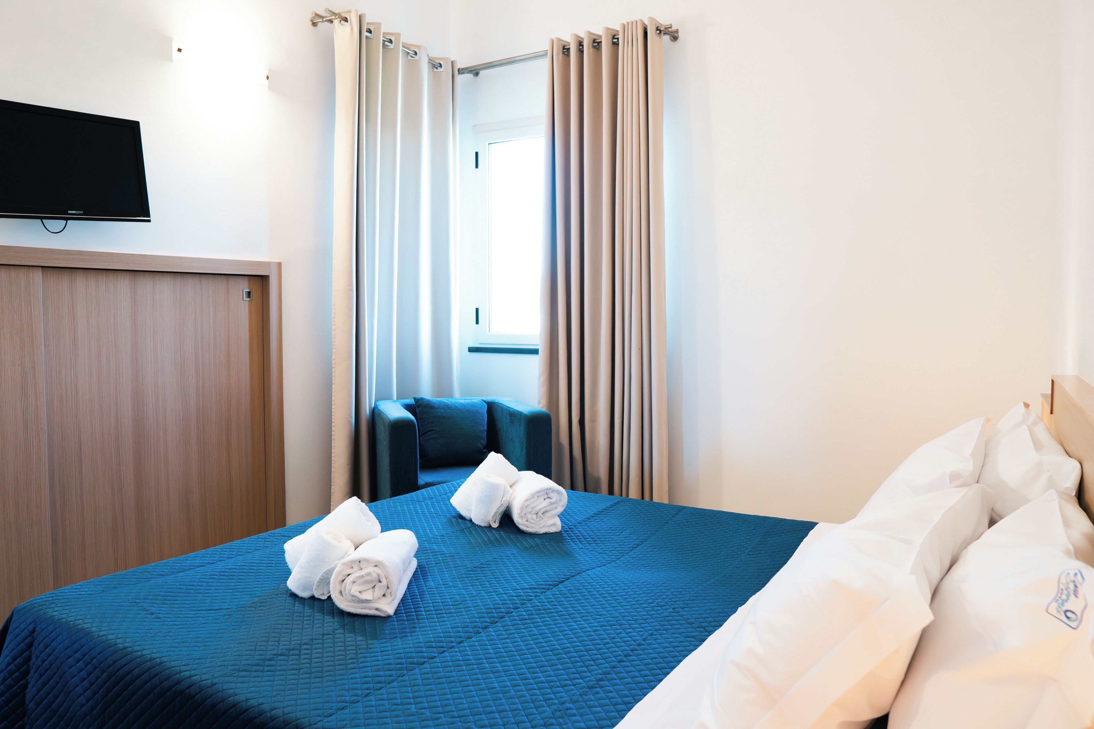 A hotel room with a bed, a TV mounted on the wall, and a window with curtains.