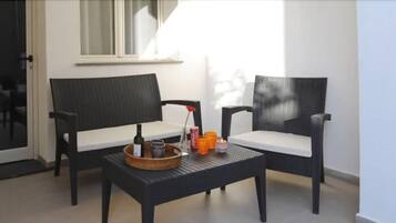 Ein Balkon mit zwei Korbstühlen, einem kleinen Tisch mit Flasche und Kerzen, sowie einer Schiebetür aus Glas.