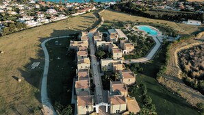 An aerial view of a coastal residential area with a row of houses, a swimming pool, and a clear view of the ocean.