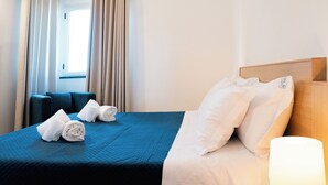 A hotel room with a neatly made bed, a bedside lamp, and a window with curtains.