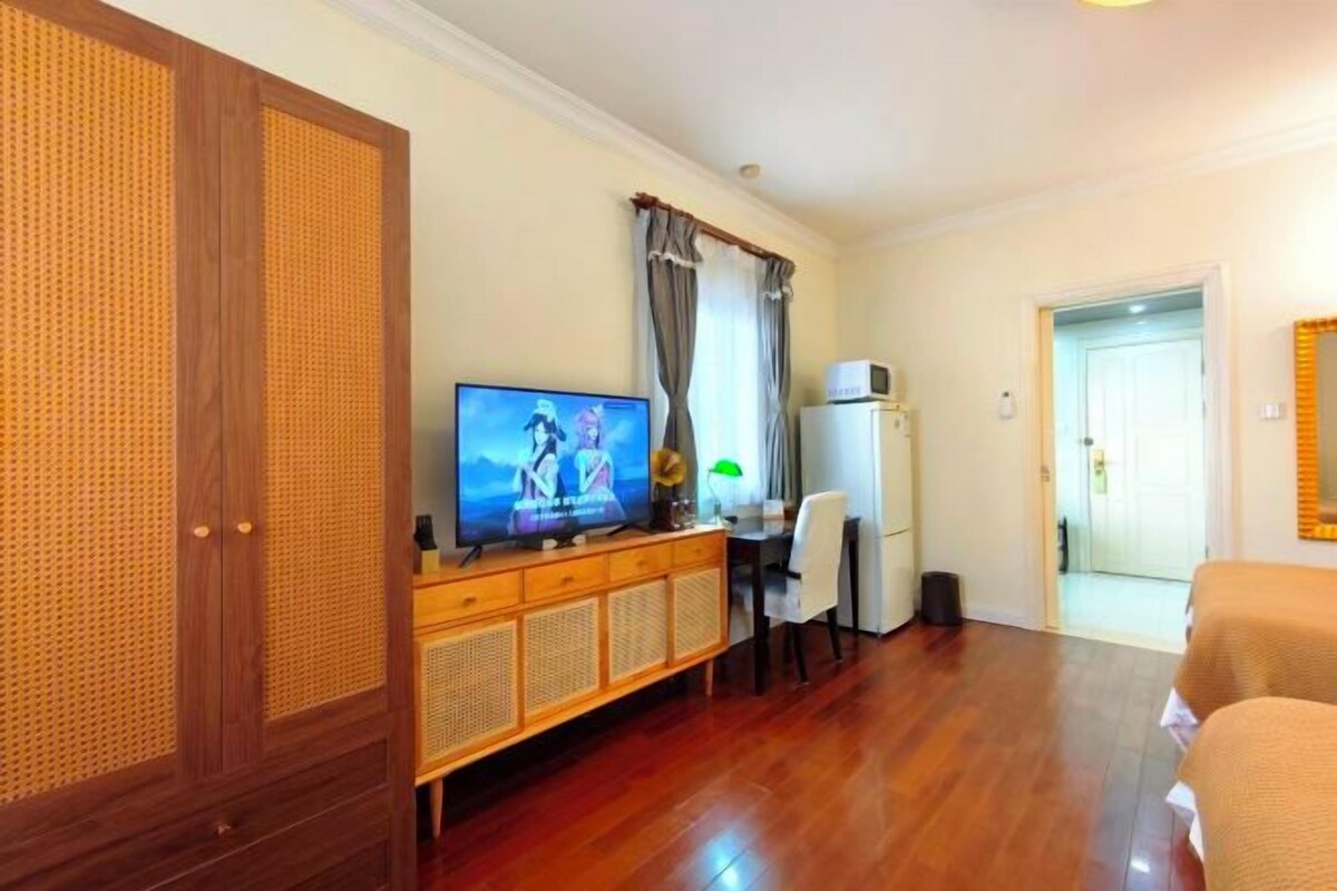 A room with a wooden cabinet, a television, a desk, a chair, and a bed.