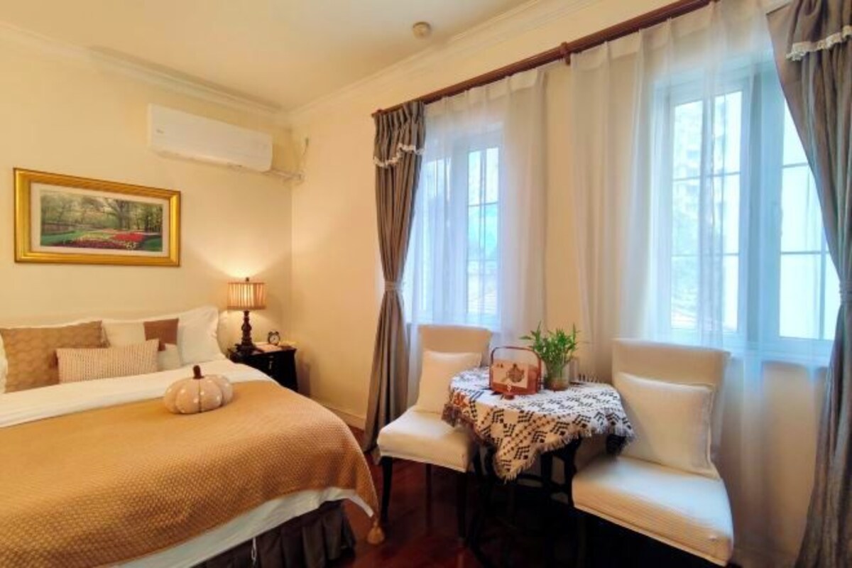 Habitación de hotel con una cama, una silla, una mesita con una planta y una ventana con cortinas.