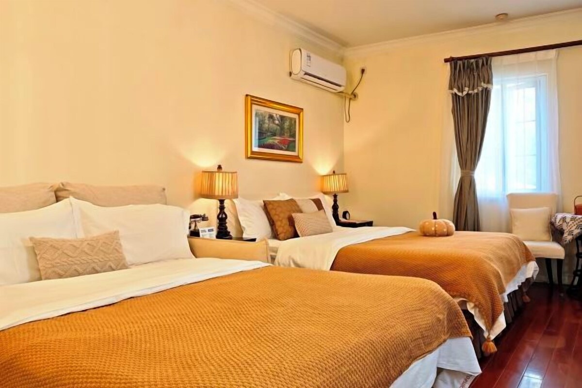A hotel room with two beds, a painting on the wall, an air conditioning unit, and a window with curtains.