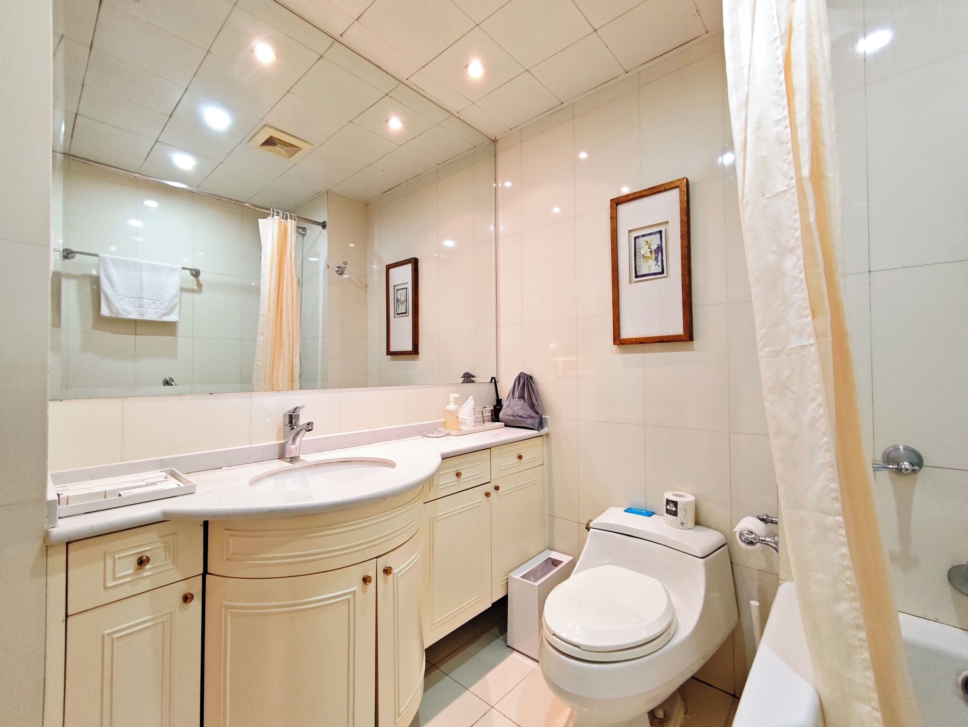 Un baño con lavamanos, espejo, inodoro y cortina de ducha.