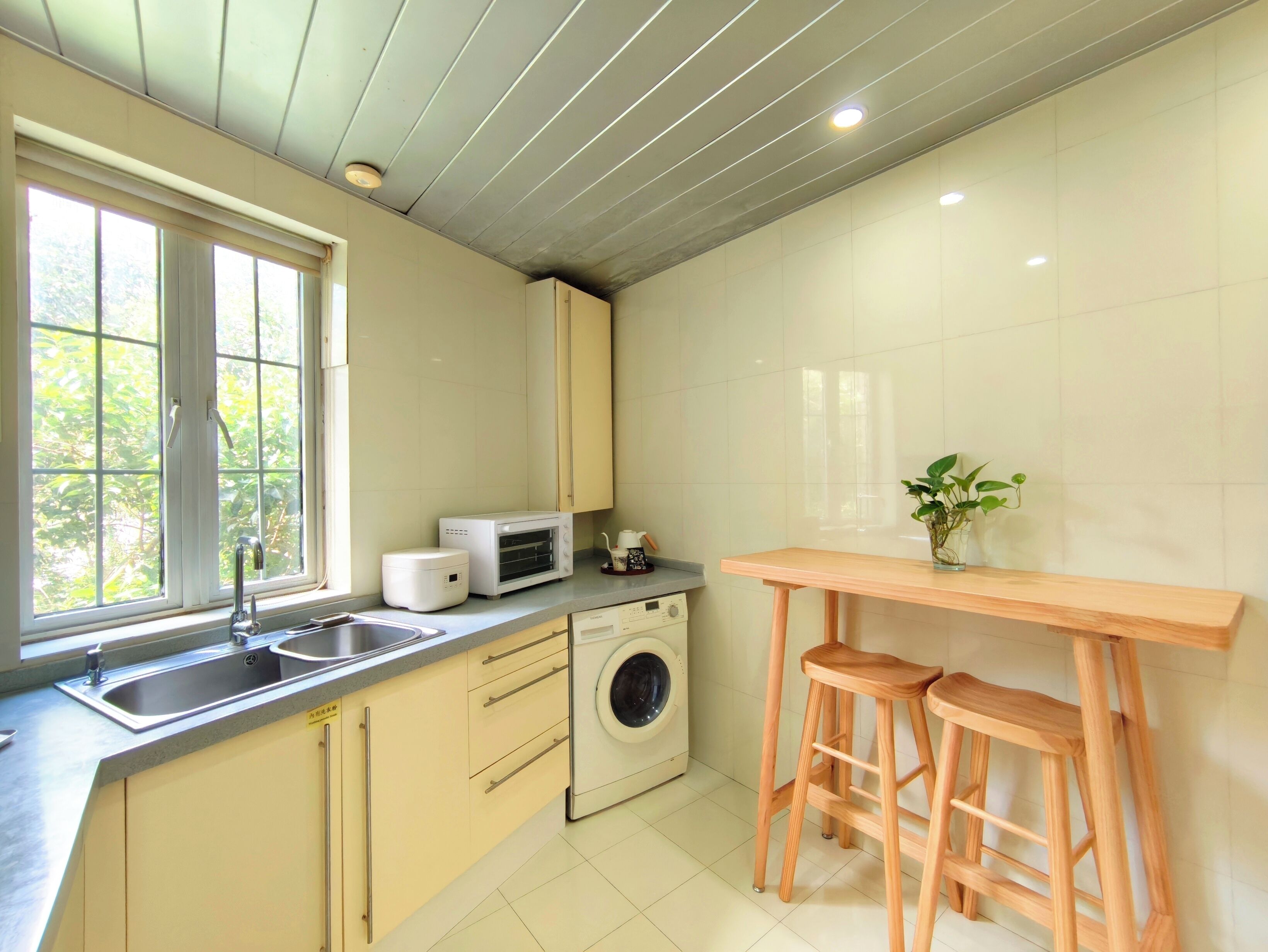 A kitchen with a washing machine, a microwave, and wooden stools.