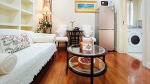 Un espacio habitable compacto con sofá, dos sillones, una mesita, lámpara, un cuadro, lavadora y refrigerador.