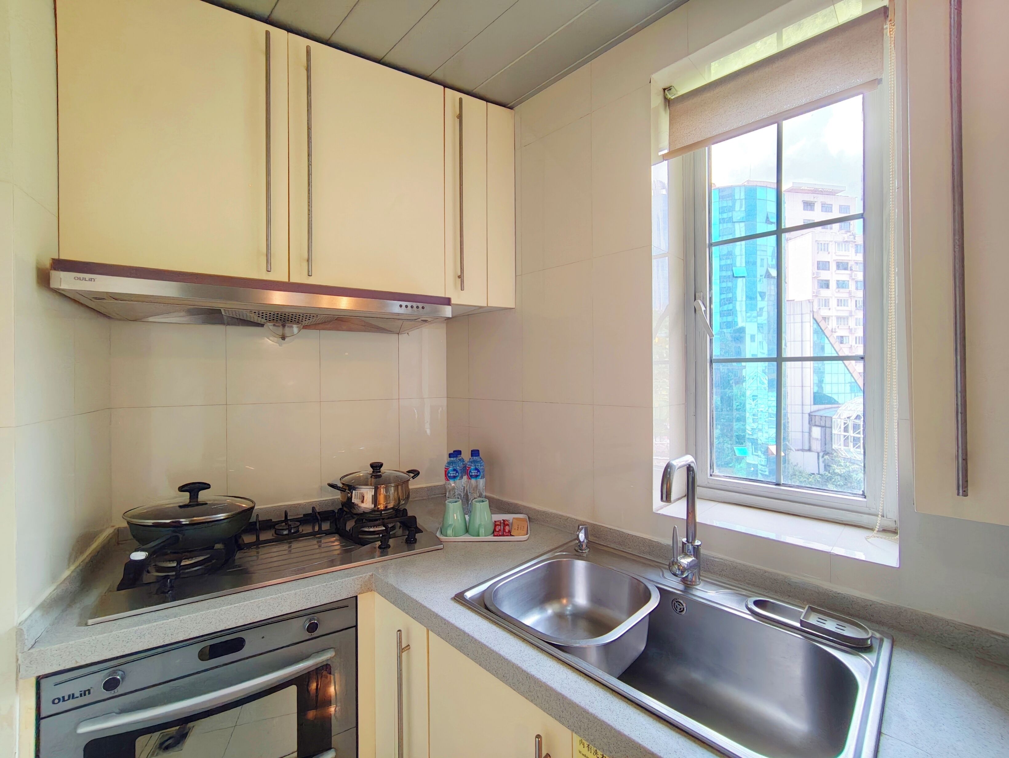 A kitchen with a gas stove, oven, stainless steel sink, and a window with a view of buildings.