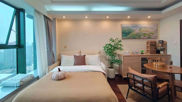 Habitación de hotel con cama, escritorio, una silla, planta en maceta y un cuadro en la pared.