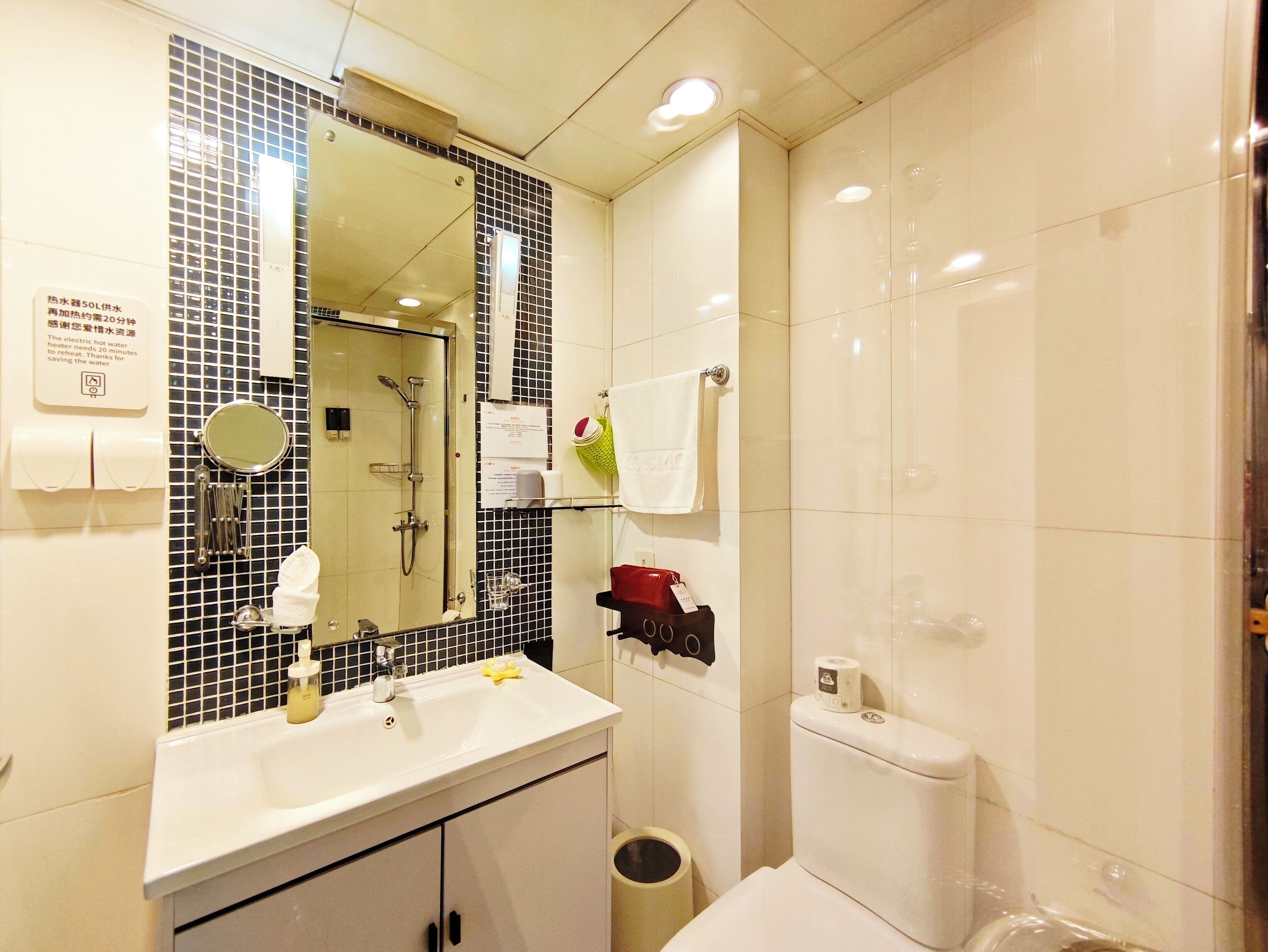 A bathroom with a sink, mirror, shower, toilet, and a trash can.