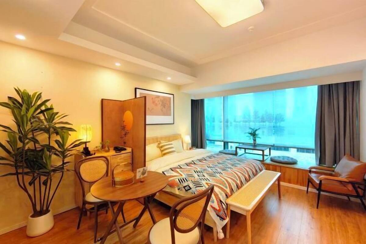 Quarto de hotel com cama, escrivaninha, cadeira, mesa de jantar e uma janela grande com vista.