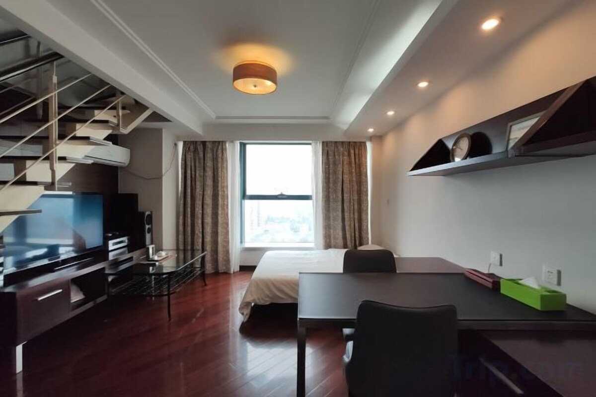 A modern hotel room with a bed, a desk, a television, and a staircase.