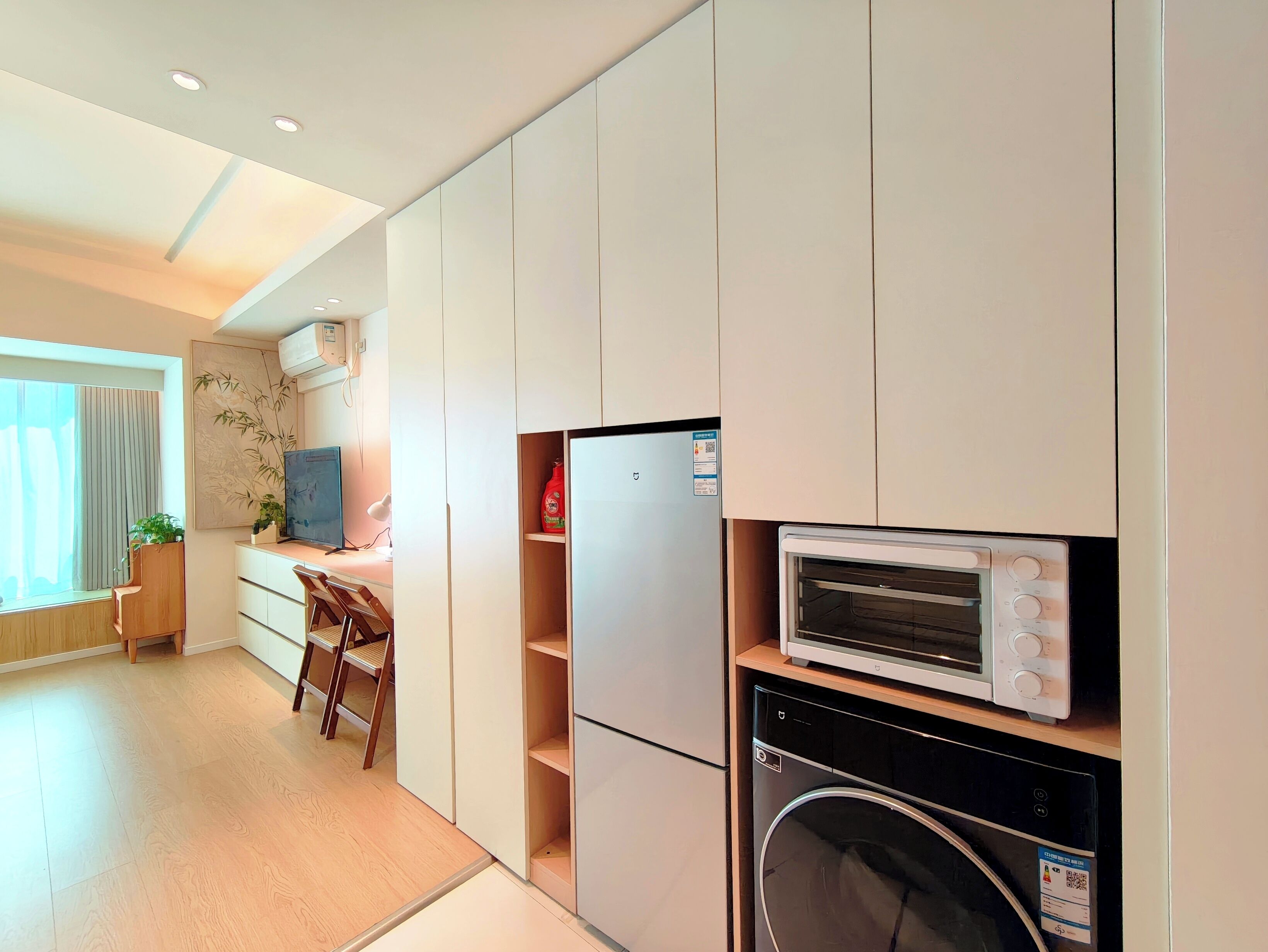 Eine moderne Küche mit eingebauten Geräten, eine Essecke mit Holztisch und -stühlen sowie ein großes Fenster mit Vorhängen.