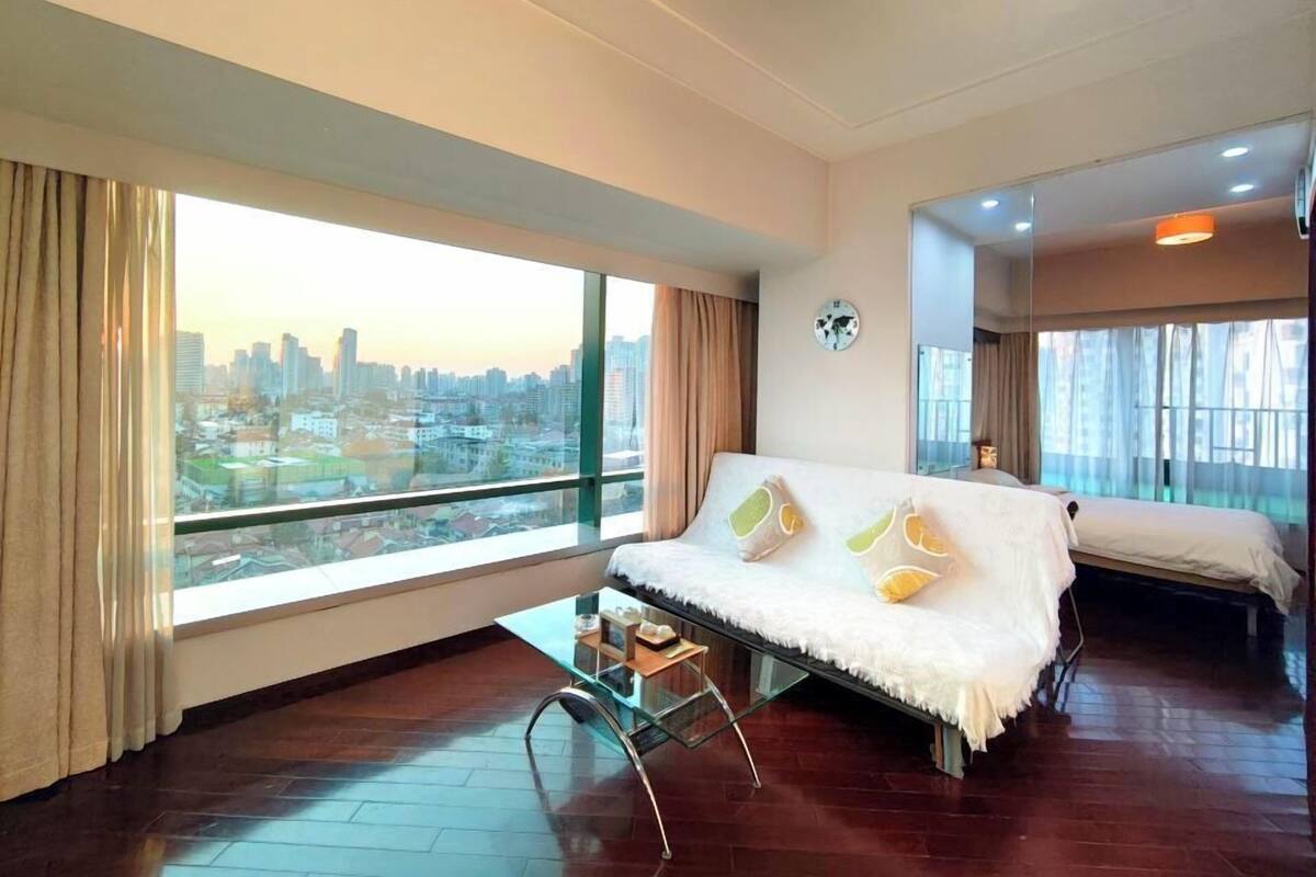 Quarto de hotel moderno com uma grande janela, um sofá, uma cama e uma pequena mesa.
