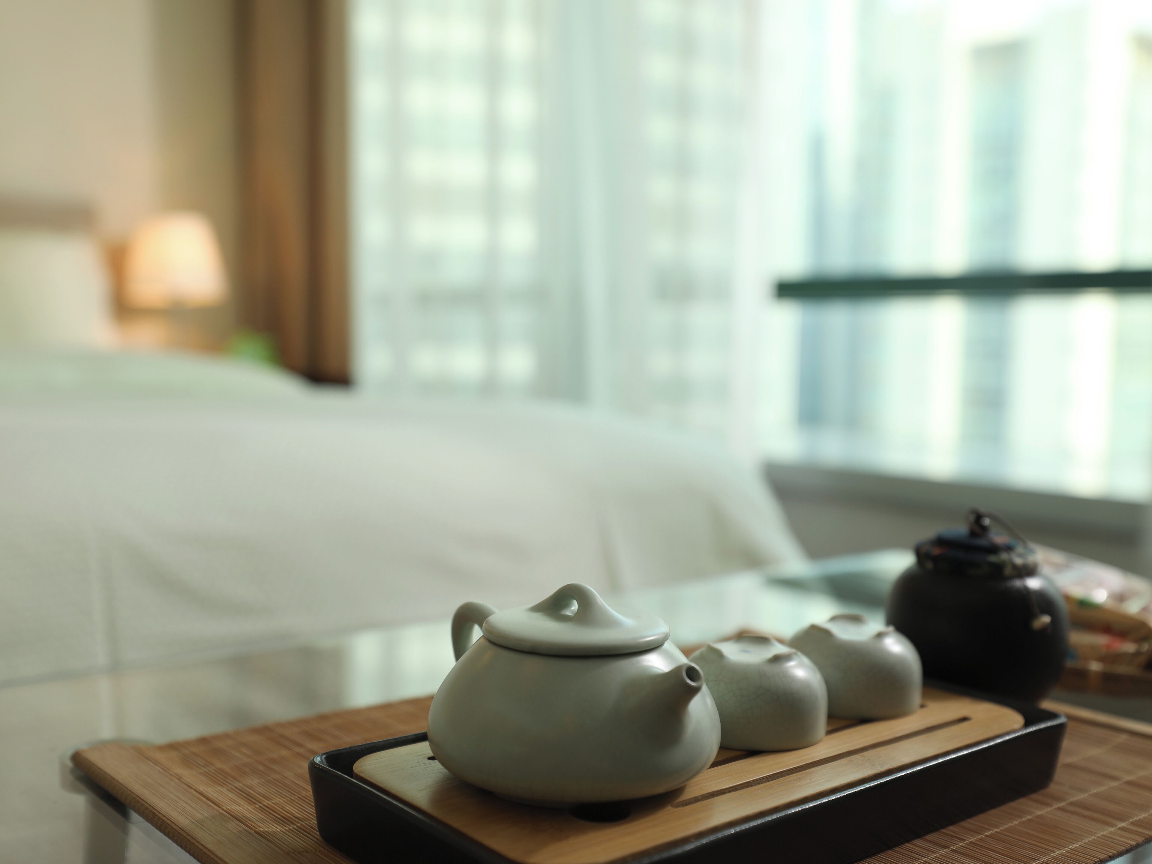 A tea set on a tray with a bed in the background.