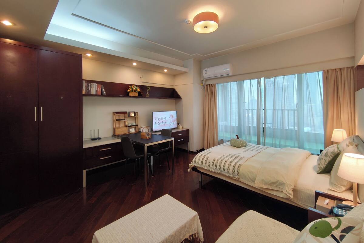 Quarto de hotel moderno com uma escrivaninha, cama, televisão e uma janela grande.