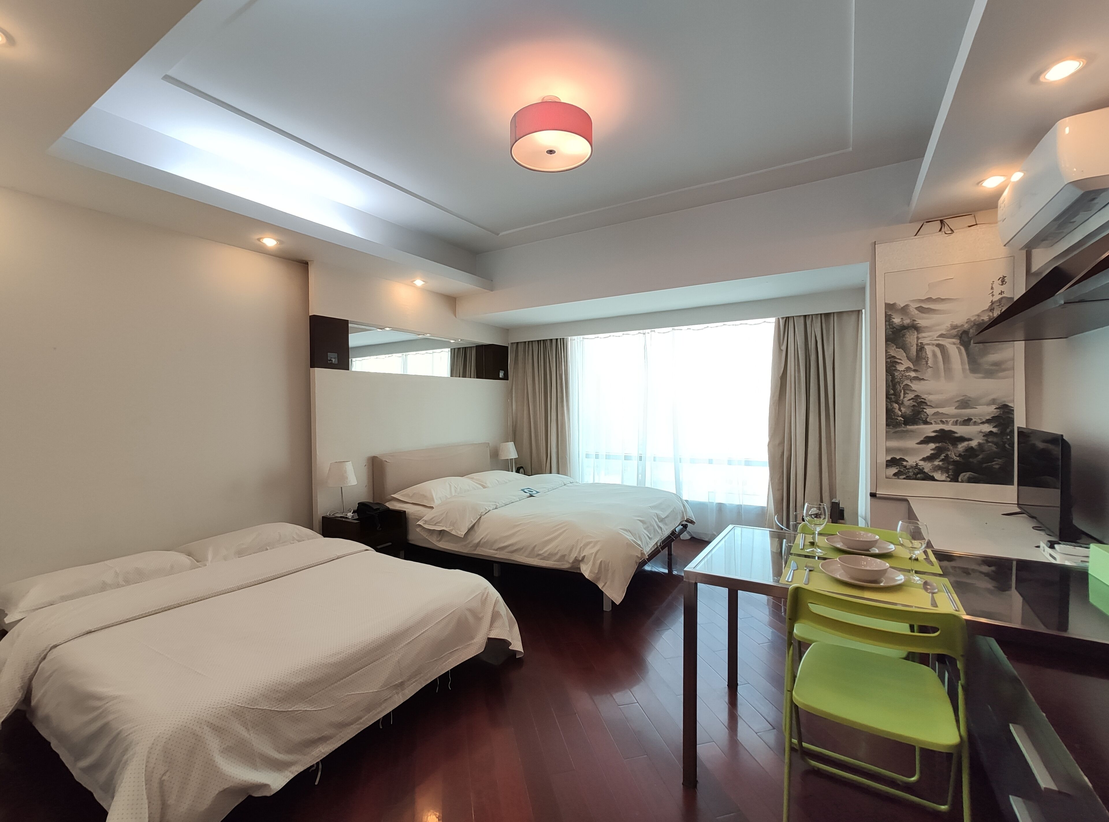 A hotel room with two beds, a dining table with chairs, a TV, and a painting on the wall.