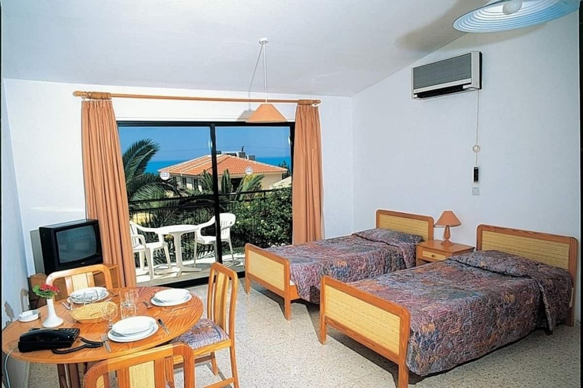 A hotel room with two beds, a dining table with chairs, a TV, and a view of the sea.