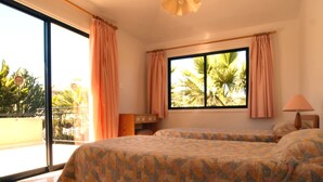 Habitación de hotel con dos camas, un balcón y un ventanal grande con cortinas.