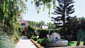 Un camino pavimentado bordeado por abundante vegetación y una jardinera de piedra con una estructura decorativa.