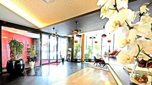 Een ruime lobby met een houten vloer, grote ramen en kamerplanten.
