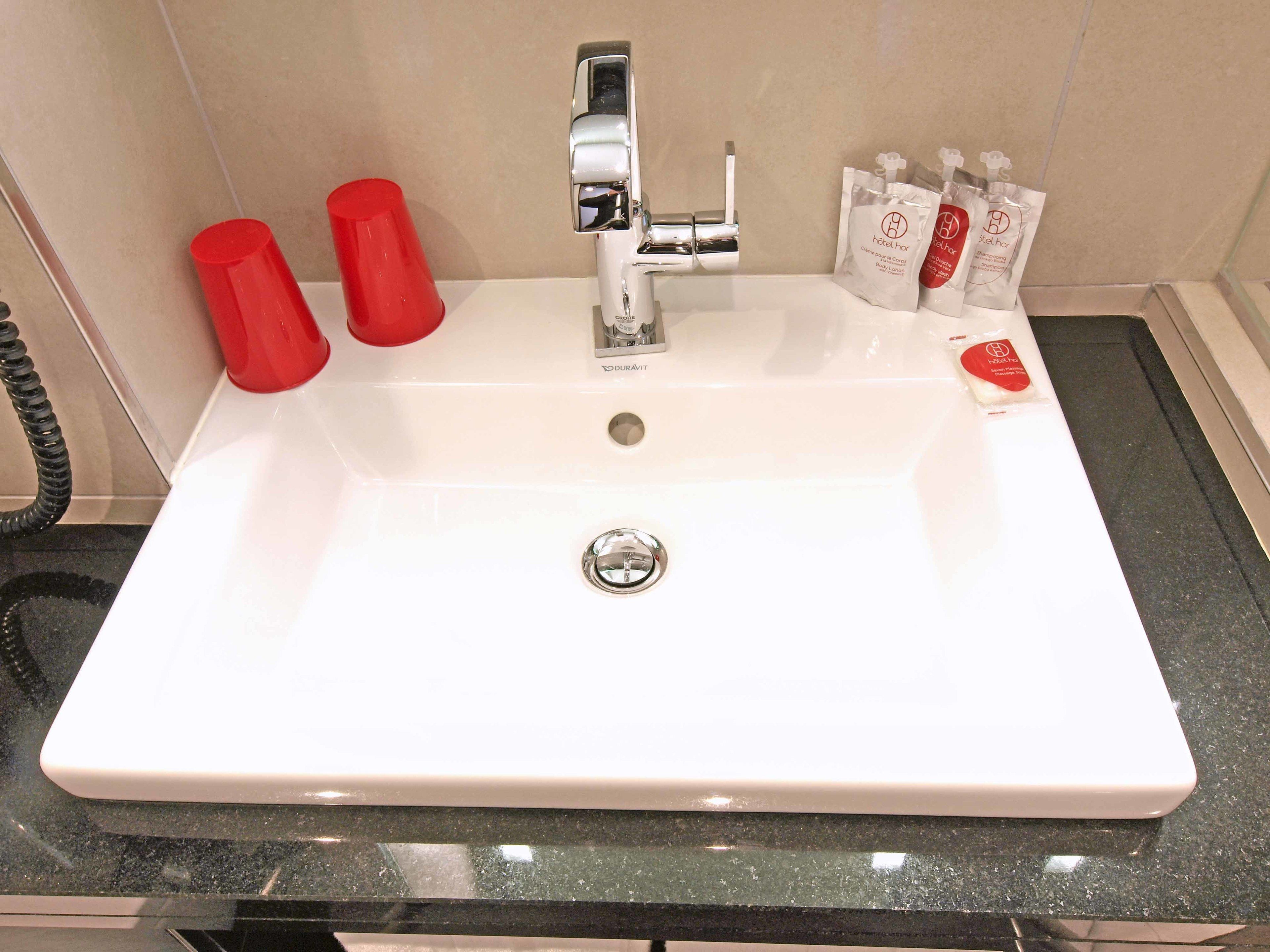 A white bathroom sink with a chrome faucet, two red soap dispensers, and a package of hotel toiletries.