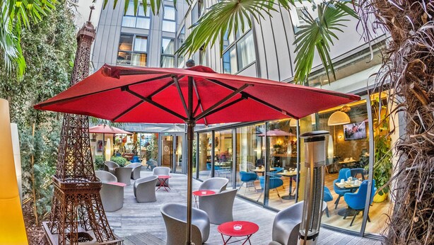 Een binnenplaats met rode parasols, moderne zitplaatsen en een decoratieve torenconstructie.