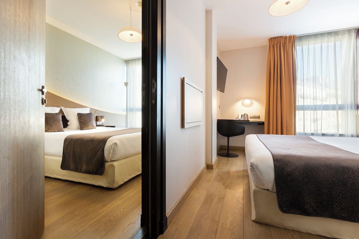 A hotel room with two beds, a desk, a chair, a TV, and a window with curtains.