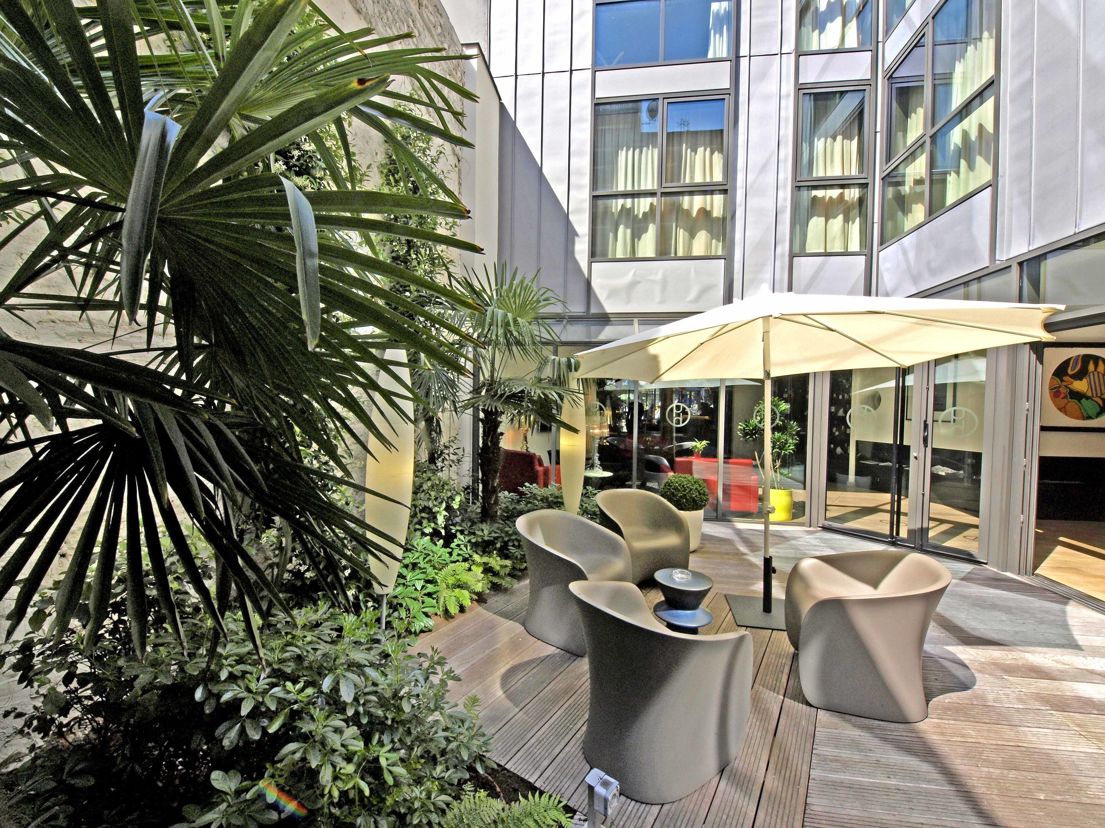 An outdoor seating area with modern furniture, surrounded by lush greenery and a glass building facade.