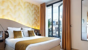Een hotelkamer met een groot bed, een nachtkastje, een lamp en uitzicht op de stad door een groot raam.