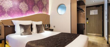A hotel room with a large bed, a round mirror, a wardrobe, and a patterned wall.