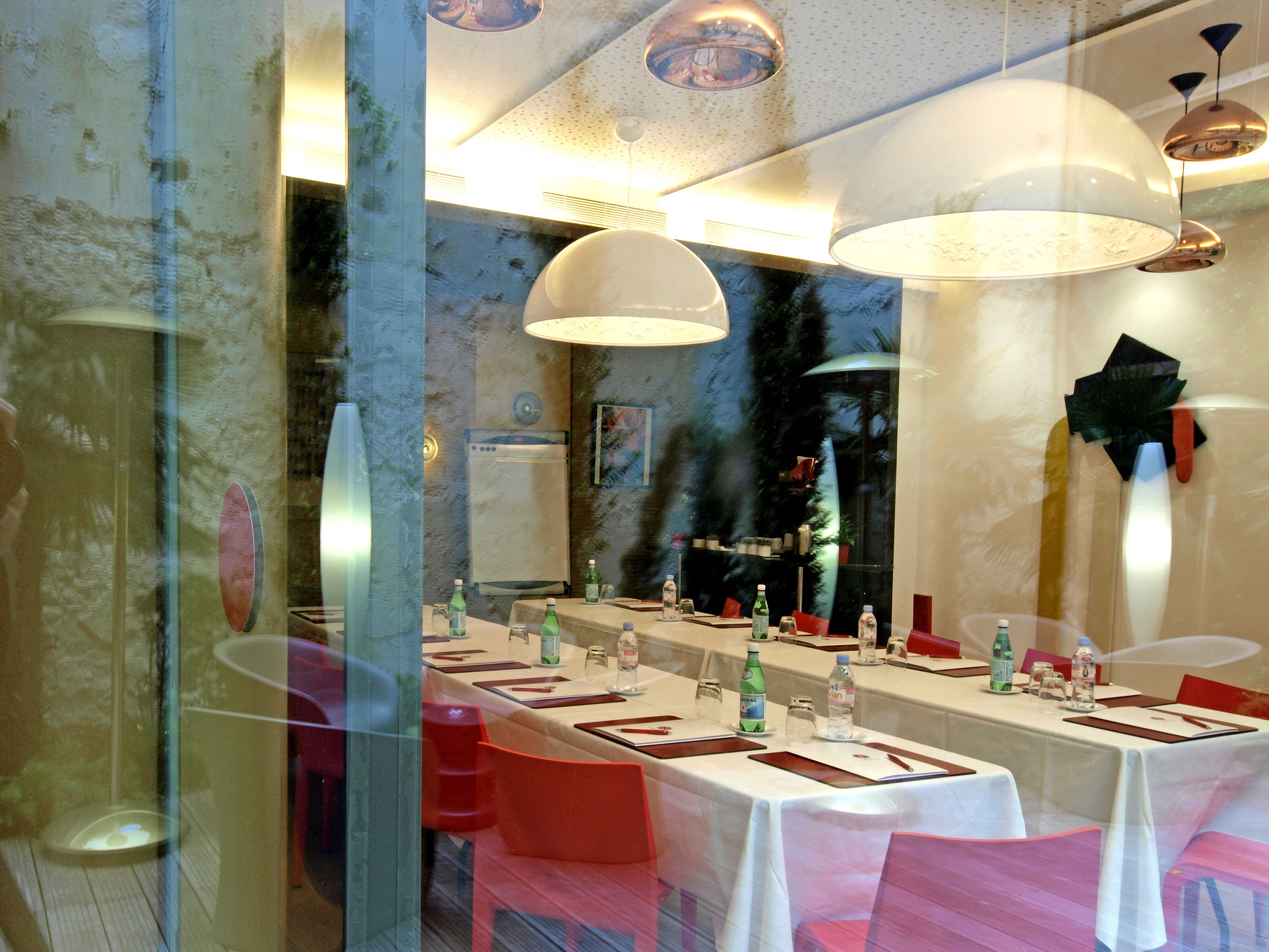 Un restaurant avec une longue table dressée pour le dîner, un lustre moderne et un grand miroir qui reflète l’intérieur.