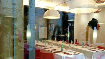 Un restaurant avec une longue table dressée pour le dîner, un lustre moderne et un grand miroir qui reflète l’intérieur.