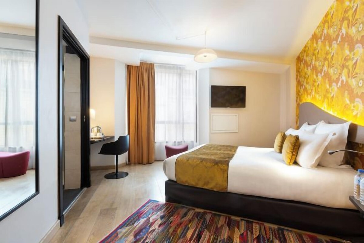 Habitación de hotel con una cama grande, un escritorio, una silla y vistas a la ciudad.