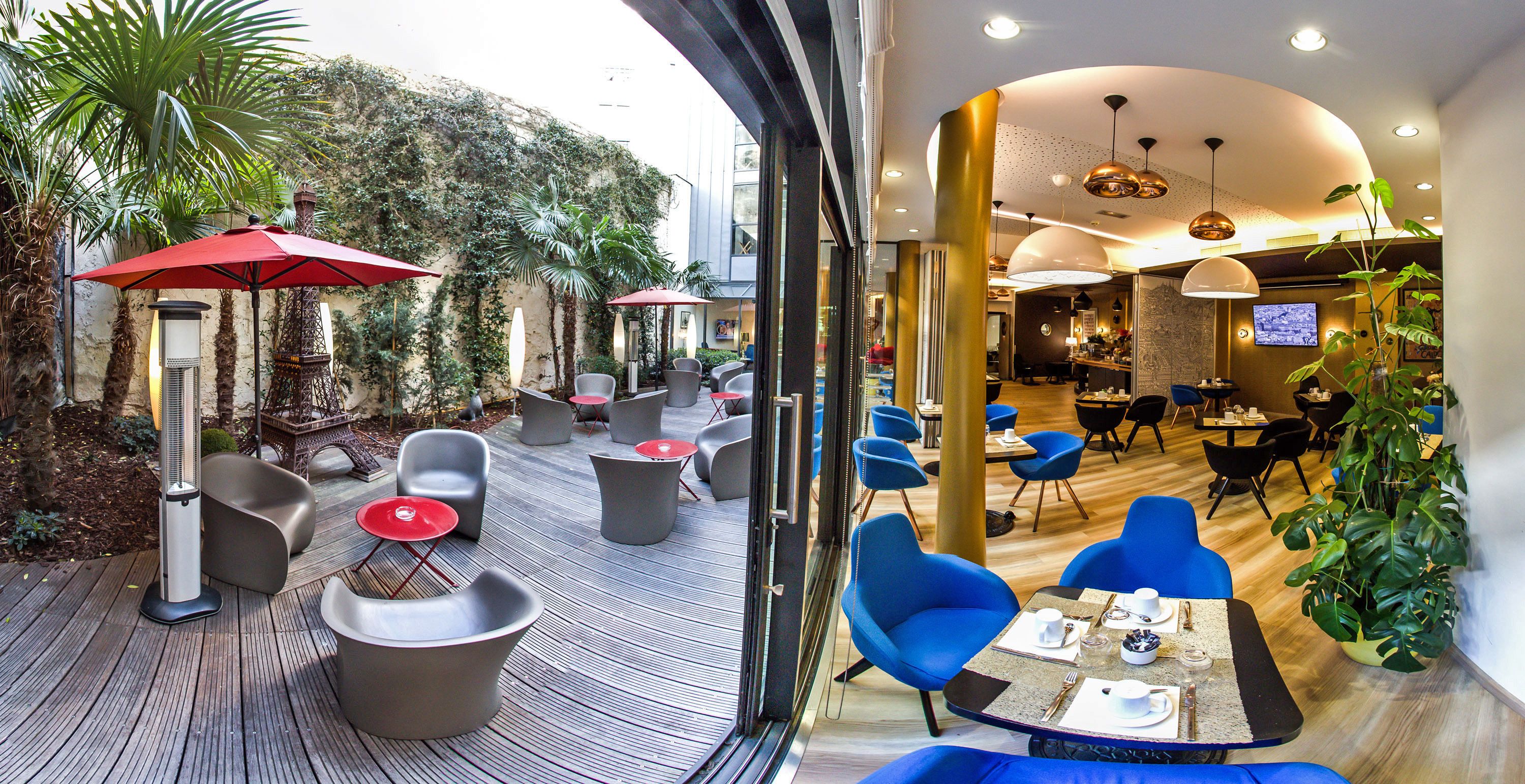 An outdoor seating area with modern chairs and red umbrellas, a wooden deck, and a view of a building with a TV.