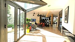 Een moderne hotellobby met glazen entree, een zithoek en een televisiescherm.