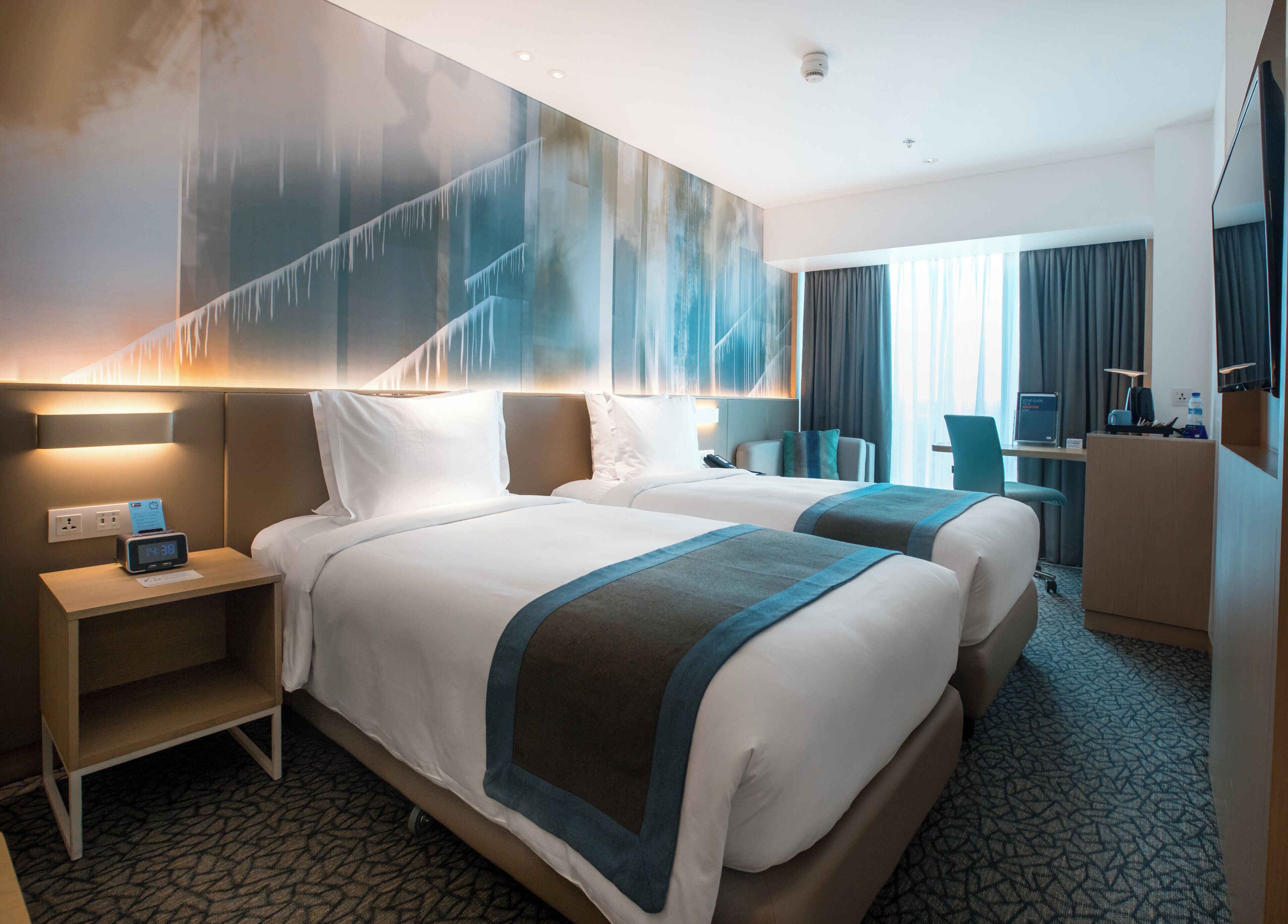 A hotel room with two beds, a desk, a chair, and a large wall mural.