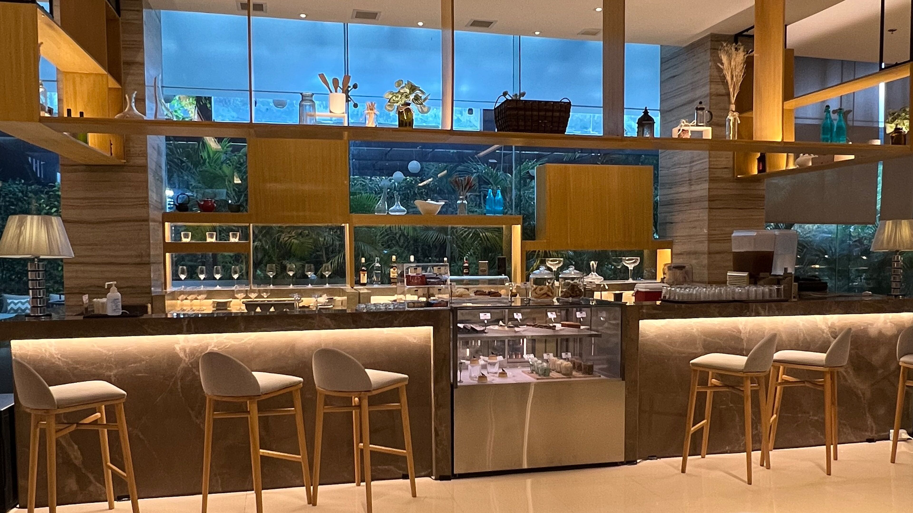 A modern bar area with a glass display case, wooden bar stools, and a view of the outdoors through large windows.