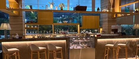 Zona de bar moderna con un expositor de vidrio, taburetes de madera y vistas al exterior a través de amplias ventanas.