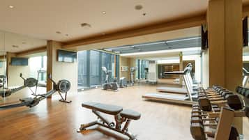 A spacious gym with various exercise equipment, large windows, and a mirrored wall.