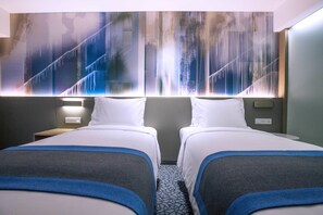 Une chambre d’hôtel avec deux lits, une grande fresque murale abstraite et une petite table de chevet avec une lampe.