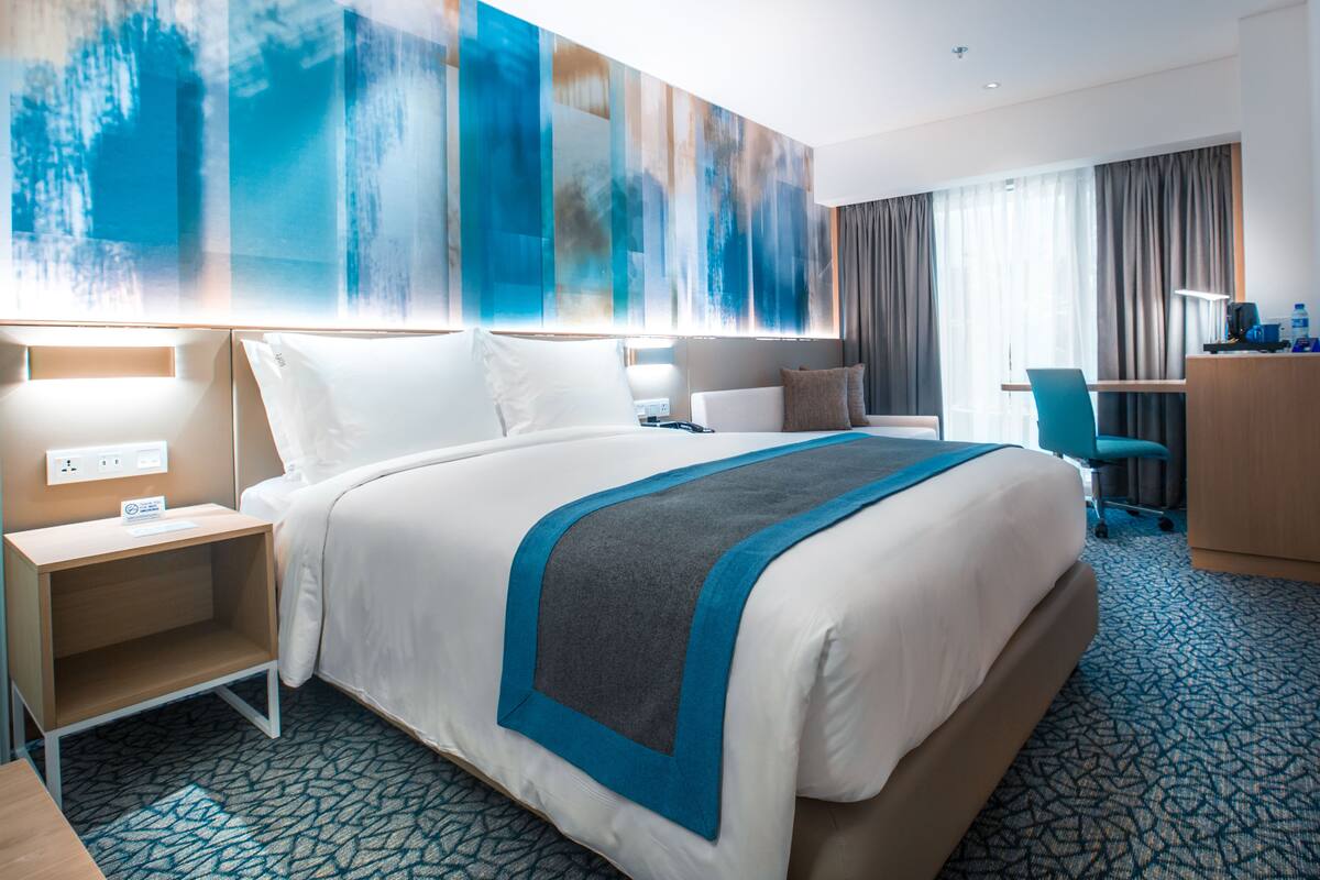 Habitación de hotel con una cama grande, un escritorio, una silla y un cuadro abstracto de grandes dimensiones en la pared.