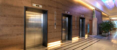 A modern elevator area with four elevators and a digital display above each.